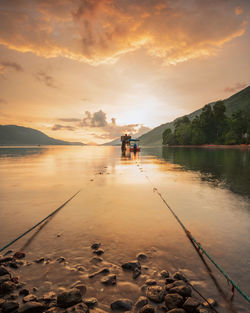 People on lake against sky during sunset