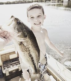 Smiling boy looking at hand holding dead fish in boat