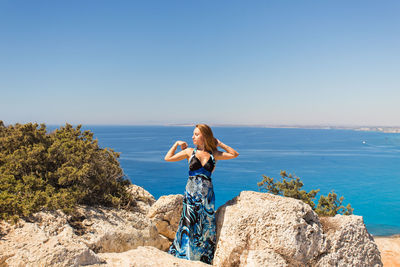 Woman standing on rock looking at sea against clear sky