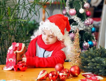 Little girl in santa claus hat rejoices and plays with christmas balls and a toy dog. 