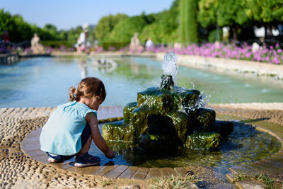 Rear view of girl crouching by fountain at park