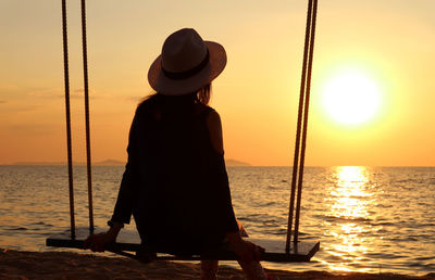 Silhouette of a woman in hat relaxing on the swing at sunset
