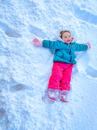 Full length of cute girl lying on snow covered land during winter