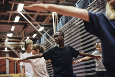 Smiling teenage boy exercising with male and female friends in sports court