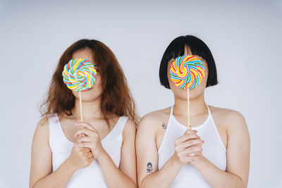 Portrait of lesbian couple holding lollipop against white background