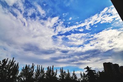 Low angle view of trees against cloudy sky