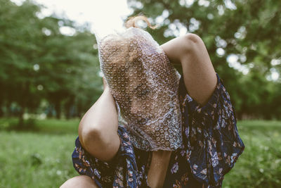 Woman covering face with bubble wrap plastic foil in park