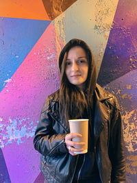 Portrait of smiling young woman standing against wall