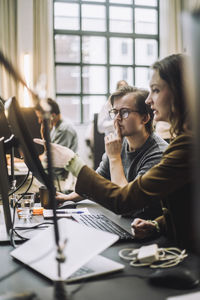 Businesswoman pointing at desktop pc while explaining to male colleague in office