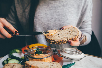 Midsection of woman applying spread on bread at home