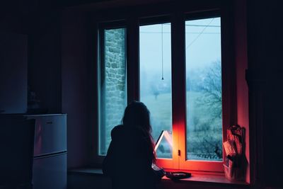 Rear view of silhouette woman sitting at window