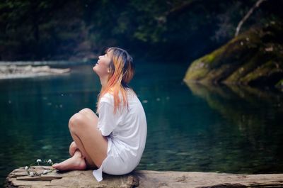 Side view of young woman sitting by lake