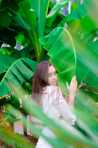 Portrait of young woman standing by banana leaf outdoors