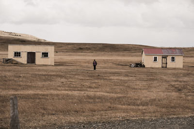 Man standing on field by building against sky