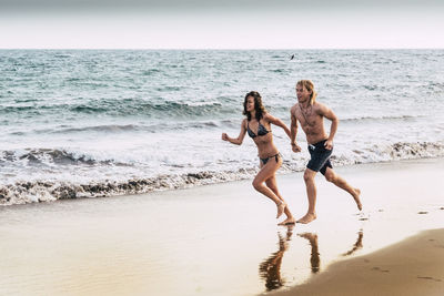 Full length of couple running at beach against clear sky