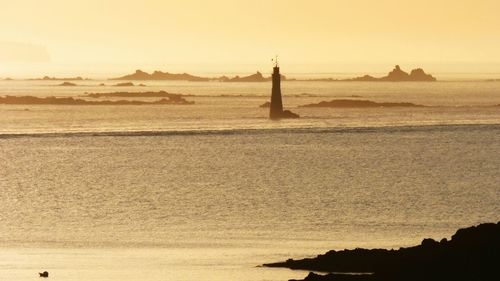 Silhouette lighthouse in sea against sky during sunset