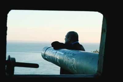 Man by sea seen through window during sunset