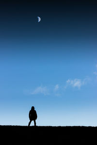 Silhouette girl standing on field against blue sky at dusk