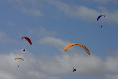 Low angle view of people paragliding against sky