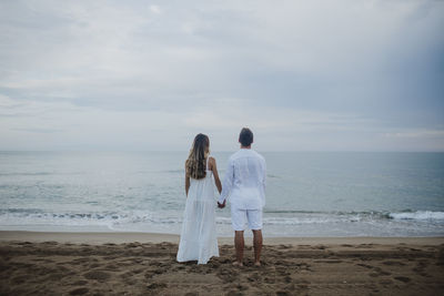 Rear view of women standing at beach against sky