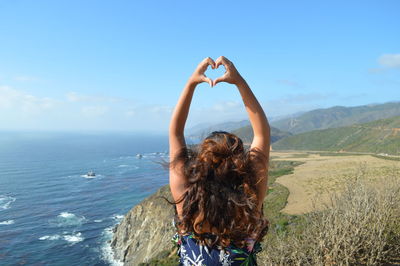 Woman making heart shape at beach against sky