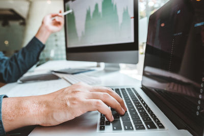 Cropped hands of business people using computers on desk