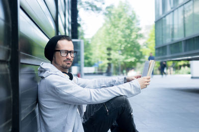 Side view portrait of mature man holding book while sitting in city