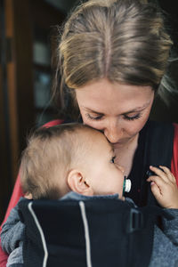 Loving mid adult mother carrying baby in carrier at home