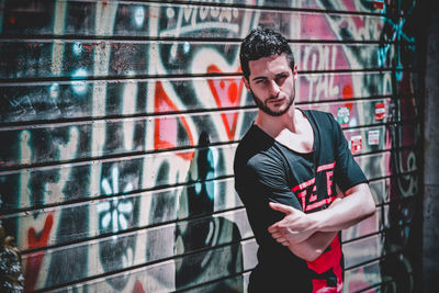 Portrait of young man with arms crossed standing against graffiti wall