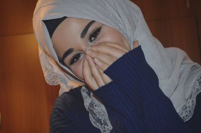 Close-up portrait of young woman in hijab hiding face with hands