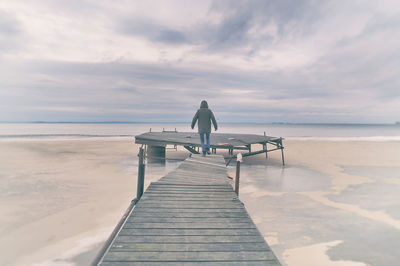 Rear view of man on pier at sea against sky