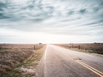 Scenic view of road amidst fields against cloudy sky