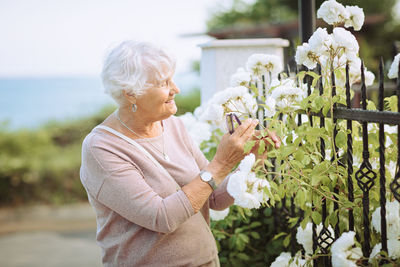 Elderly woman admiring beautiful bushes with colorful roses.