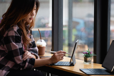 Young creative designer holding stylus pen drawing on screen of digital tablet at cafe