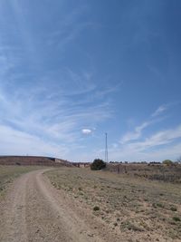 Dirt road on field against sky