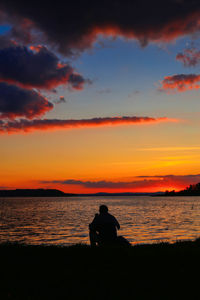Rear view of silhouette man sitting on beach against sky during sunset