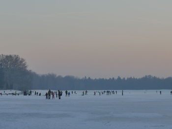 People on snowy landscape against sky during sunset