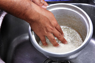 Midsection of woman washing rice in container at sink