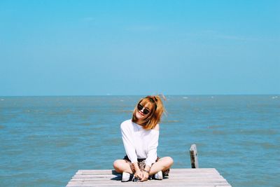 Portrait of smiling woman sitting on pier over sea against clear sky