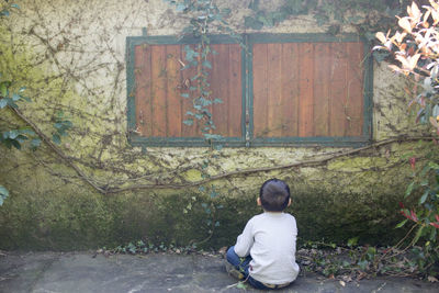 Rear view of boy sitting against building