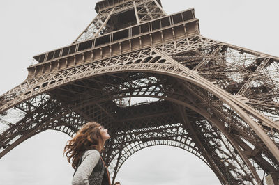 Low angle view of woman standing under eiffel tower against sky