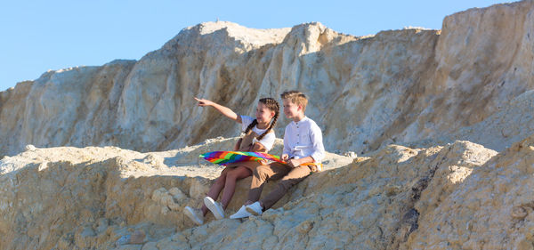 Girl pointing into the distance her friend pointing her finger while sitting high mountain. person