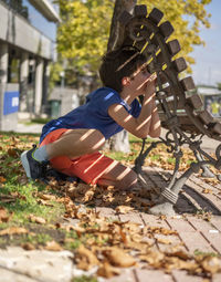 Boy playing hide and seek. looking through a gap in a wooden park bench.