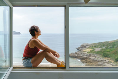 Portrait of young woman sitting on window