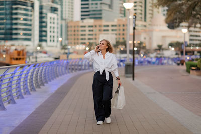 A young woman on the street with shopping bags talking on a mobile phone