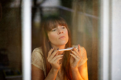 Close-up of thoughtful woman with bangs looking away seen through window