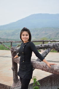 Portrait of young woman standing by railing on observation point against sky