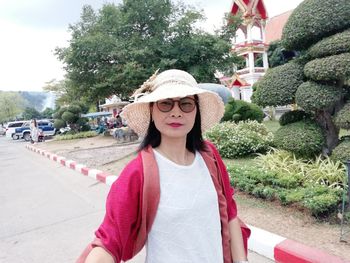 Portrait of mature woman wearing hat and eyeglasses while standing on road