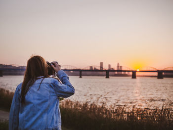 Rear view of woman photographing river during sunset