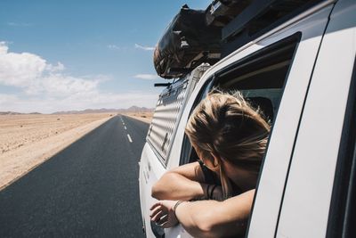 Woman looking through car window against sky